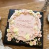 Top view of a pink floral birthday cake with pastel yellow and pink cream flowers, green vines, little hearts and Happy Birthday lettering