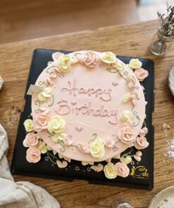 Top view of a pink floral birthday cake with pastel yellow and pink cream flowers, green vines, little hearts and Happy Birthday lettering